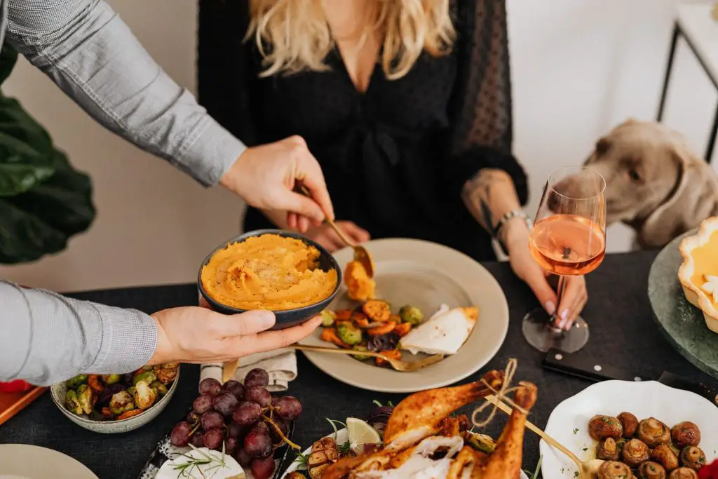 People and a Dog at a Dinner Table with Variety of Food